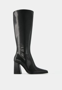 Black leather knee-high boot with a pointed toe and chunky block heel. Smooth texture with a glossy finish and minimalistic design.