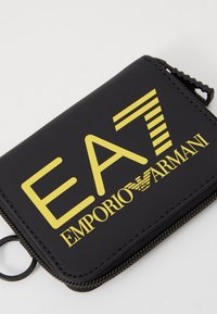 Juodas su užtrauktuku piniginė su geltonu "EA7 EMPORIO ARMANI" logotipu. Pasižymi glotnia tekstūra ir raktų laikikliu. Kompaktiškas dizainas.