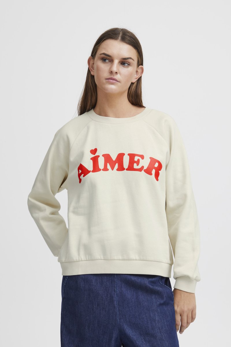 Cream sweatshirt with red "AIMÉR" text, raglan sleeves, ribbed cuffs, and hem, made from soft fabric with a smooth texture.