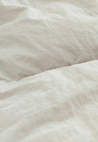 Linnedynen med en blød, krøllet tekstur i lys beige. Subtile farvevariationer skaber et naturligt udseende uden mønstre eller accenter.