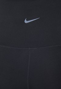 Leggings de sport noirs avec un logo Nike en gris clair. Le tissu est lisse avec des coutures à plat et une taille haute.