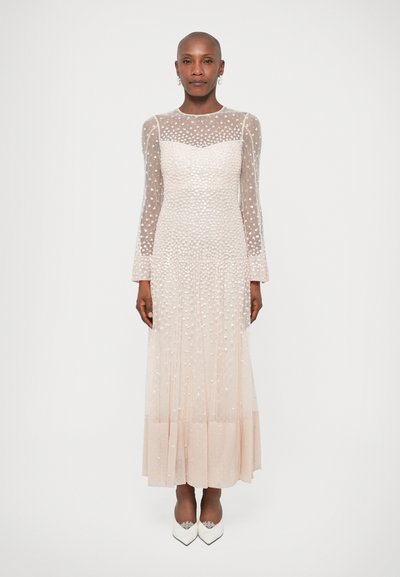 Robe transparente à manches longues de couleur beige clair avec des détails texturés en pois. Buste ajusté, jupe fluide et ourlet lisse, accompagnée de chaussures blanches.
