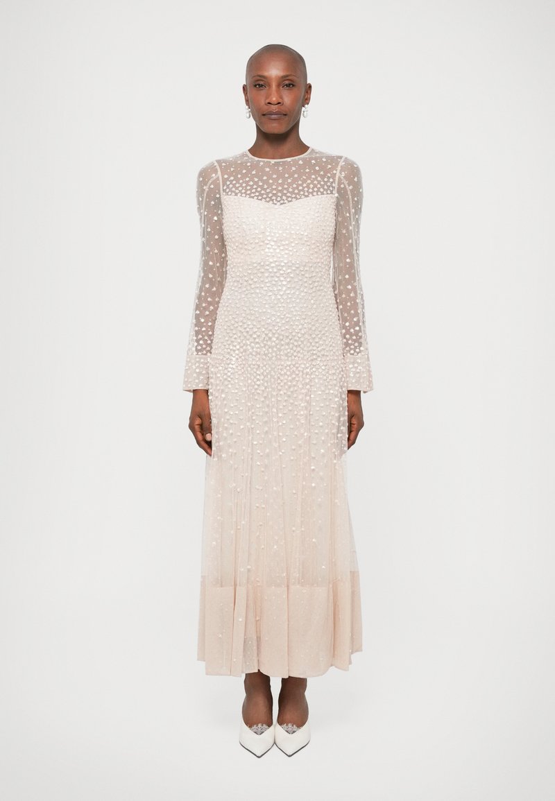 Prozirna haljina dugih rukava u svijetloj bež boji s teksturiranim točkastim detaljima. Prilagođen gornji dio, lepršava suknja i glatki rub, u paru s bijelim cipelama.