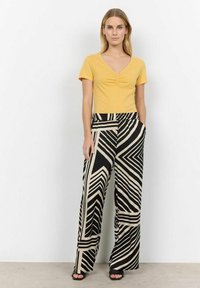 Yellow, short-sleeve V-neck top paired with black and beige wide-leg pants featuring a geometric striped pattern. Model stands on a light background.