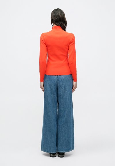 Haut en maille orange à manches longues avec un col haut, associé à un pantalon en denim bleu à jambes larges. Texture lisse et design simple, vu de dos.