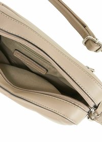 Bolso cruzado de cuero beige con cierre de cremallera. El interior cuenta con un forro de tela suave y una etiqueta. Correa ajustable visible.