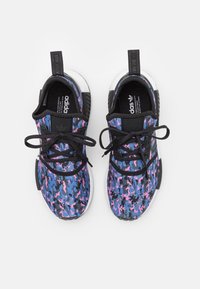 Ett par Adidas sneakers med blå, rosa och svart camouflage-mönster, svarta snören och vita mellansulor sedda uppifrån mot en vit bakgrund.