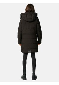 Black puffer coat with a hood, featuring a quilted pattern, and a mid-thigh length. Worn with black skinny jeans and black boots.