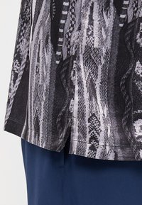 Black and white patterned top, featuring a smooth texture and a slight split at the hem, paired with dark blue pants.