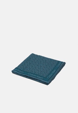 Écharpe bleue Calvin Klein pliée avec un motif texturé et le nom de la marque le long des bords sur fond blanc.