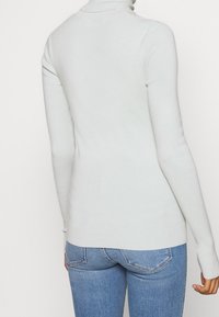 Pull à col roulé gris clair avec manches longues, texture côtelée et coupe ajustée, associé à un jean bleu taille mi-haute.