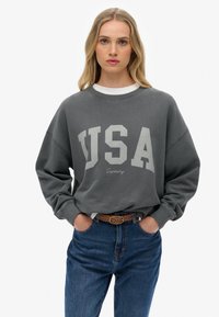 Grijze oversized sweatshirt met "USA" in grote off-white letters, voorzien van een ronde hals en ribgebreide manchetten, gecombineerd met blauwe denim.