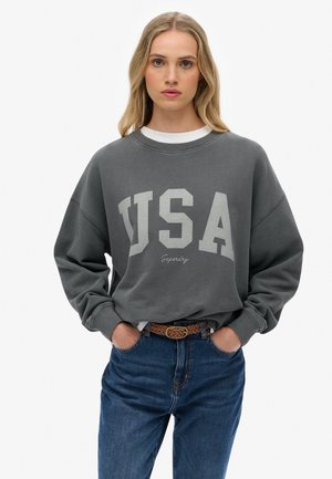 Gray oversized sweatshirt featuring "USA" in large off-white letters, with a crew neckline and ribbed cuffs, paired with blue denim.