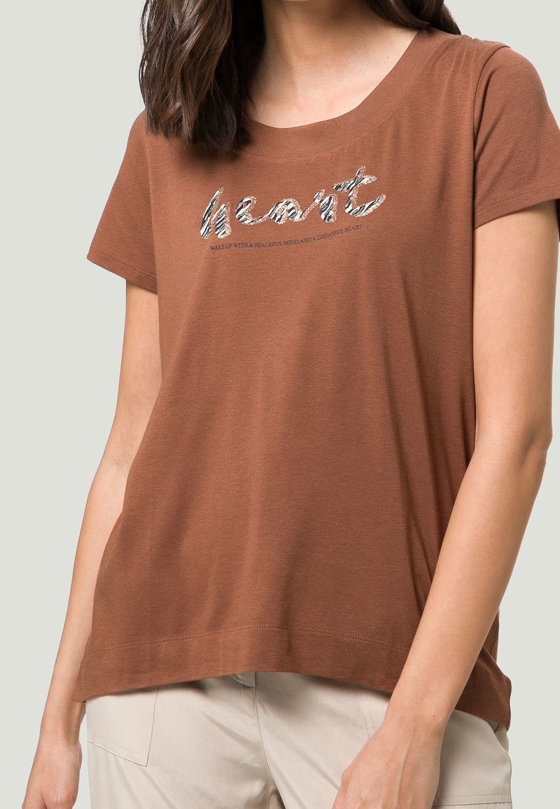 Brun bomulds t-shirt med korte ærmer, der har et metalagtigt tekstgrafik, som står "hjerte" og yderligere tekst nedenfor. Blød tekstur.