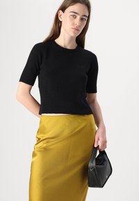 Must mustriga must-sweater lühikeste varrukatega, pehme tekstuur ja ribaga allserva, koos siidise kuldse-kollase seeliku ja väikese musta käekotiga.