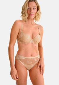 Reggiseno beige con pizzo, dotato di ferretto e spalline regolabili, abbinato a una mutanda alta coordinata con ricami floreali e rete trasparente.