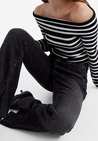 Zwart-wit gestreepte off-the-shoulder ribbed top gecombineerd met hoogwater zwarte jeans en zwarte hakken met bandjes.