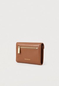 Bruine leer wallet met een gestructureerd uiterlijk, voorzien van een gouden ritszak aan de voorkant en het gouden "COCCINELLE" logo op een neutrale achtergrond.