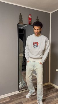 Gray sweatshirt featuring a graphic design, paired with light blue jeans and silver sneakers. The setting includes a mirror and simple decor.