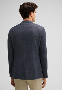Marinefarbener Blazer mit strukturierter Oberfläche und taillierter Passform, mit zurückgesetzten Revers und einem Schlitz hinten. Er hat knöpfbare Manschetten und eine minimalistische Gestaltung.