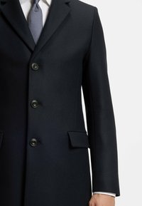 Cappotto in lana navy con vestibilità su misura, dotato di revers a punta, quattro bottoni e tasche a pattina. Texture liscia e design sobrio.