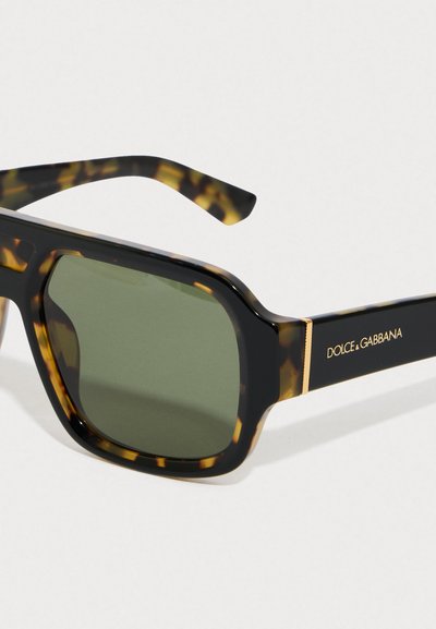 Sklenice s obdélníkovým tortoiseshell rámem, zelenými skly a černými stranami, zdobené zlatým logem Dolce & Gabbana.