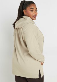 Felpa beige con cappuccio, dal taglio rilassato, con spacchi laterali e polsini a costine. Texture morbida con sottili dettagli di cucitura sulle cuciture.