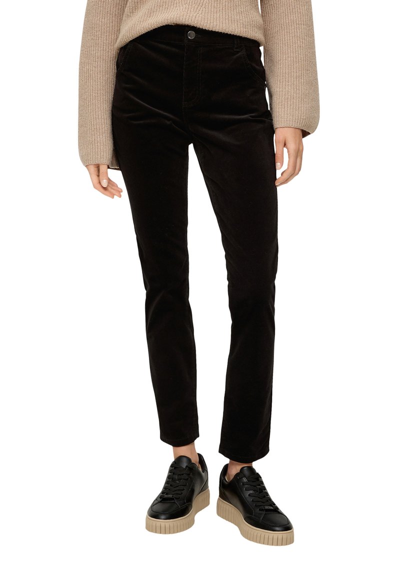 Pantalons en velours côtelé noir avec une coupe slim, dotés d'une fermeture à bouton et de poches, associés à des baskets noires texturées et un pull en tricot beige.