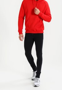 Červená mikina s kapucí a přední kapsou, kombinovaná s černými slim-fit džíny a šedými teniskami. Hladká tkanina, ležérní design a nastavitelné šňůrky.