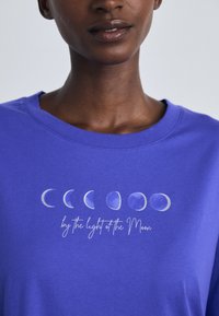 Sweatshirt de algodão roxo com gráficos das fases da lua e o texto "à luz da lua" em uma fonte casual. Textura suave.