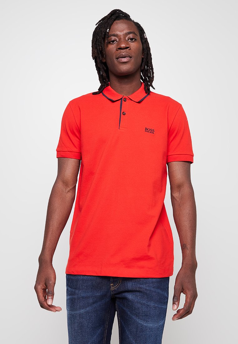 Polo shirt rouge en coton avec un col à boutons, deux boutons, et une bordure marine sur le col, arborant un petit logo sur la poitrine.