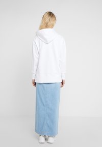Sudadera blanca con capucha de corte relajado, combinada con una falda maxi de mezclilla azul claro. Texturas suaves y diseño sencillo.