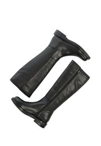 Czarne skórzane kozaki do kolan o gładkiej fakturze, z bocznymi zamkami błyskawicznymi i niskimi obcasami. Charakteryzują się eleganckim, przylegającym do ciała fasonem.