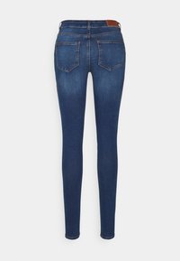 Jeans ajustados de mezclilla azul oscuro con una textura suave. Presenta dos bolsillos traseros y un discreto parche de cuero marrón en la cinturilla.