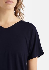Top blu navy a maniche corte con scollo a V, realizzato in tessuto morbido con vestibilità rilassata, caratterizzato da una texture liscia e dettagli delle cuciture minimali.