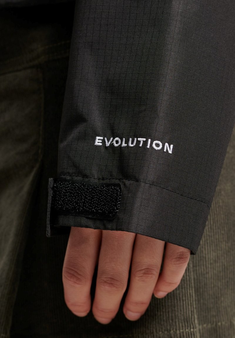 Zwarte stoffen jacksleeve met een gestructureerd ruitpatroon, voorzien van een witte geborduurde "EVOLUTION" logo en een zwarte klittenbandsluiting.