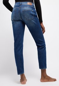 Dunkelblaue Jeans aus Denim mit slim Fit, mittelhoher Taille und fünf Taschen. Mit einem Leder-Brandpatch am hinteren Bund.