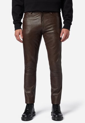 Braune Lederhose mit glatter Textur, schmalem Schnitt, fünf Taschen und detaillierten Nähten, kombiniert mit schwarzen Schnürstiefeln.