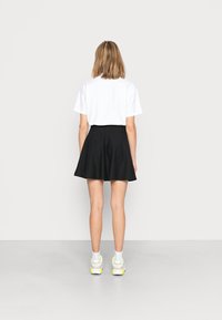 Vit kortärmad t-shirt kombinerad med en svart utsvängd kjol. Vita ankelsockor och sneakers med neondetaljer fulländar stilen.