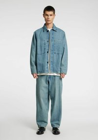 Svetlomodra denim jakna z gumbno zapenjanjem, enim prsni žepom in širokimi kavbojkami. Oblečena čez belo majico in črne čevlje.