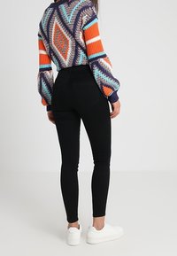 Jeans negros ajustados de cintura alta, combinados con un suéter de punto multicolor con patrones geométricos. Zapatillas blancas completan el look.