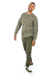 Maglione verde e nero con texture abbinato a pantaloni cargo olivastro e sneakers verdi. Presenta una vestibilità comoda e un tessuto confortevole.