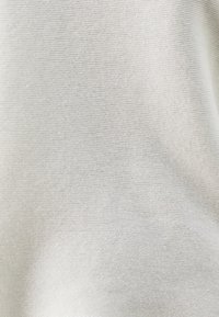 Vaaleanharmaa neulottu kangas, jossa on hieno rakenne ja hillitty kuviollisuus, joka korostaa sen pehmeää ilmettä. Yksityiskohtainen, sileä pinta.