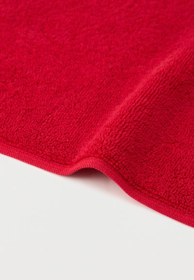 Lys rød frottéstof med en blød, løkkeagtig struktur og en let hævet kant på en hvid baggrund.