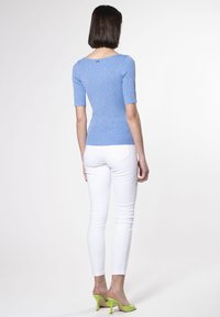 Top de punto acanalado azul claro con escote barco y mangas cortas, combinado con pantalones ajustados blancos y sandalias de tacón verdes.