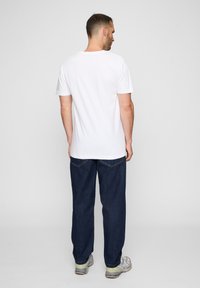 Balta medvilnė t-shirt su trumpomis rankovėmis, derinama su laisvais tamsiai mėlynais džinsais. Matoma siuvimo detalė ant džinsų.