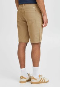 Khaki shorts med lige snit, to baglommer og dekorativ syning. Båret med hvide sokker og beige sneakers med brune accenter.