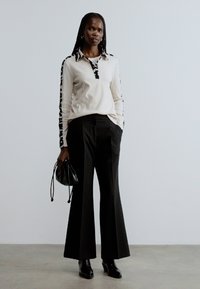 Krämfärgad långärmad topp med svarta detaljer, kombinerad med svarta vida byxor. Svart handväska, eleganta svarta skor. Enkel, modern design.