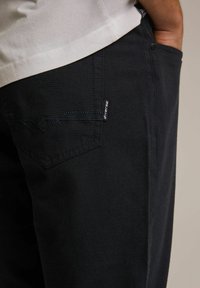 Granatowe spodnie z płótna o teksturowanej powierzchni, z tylną kieszenią z kontrastowym przeszyciem i małą metką z logo.