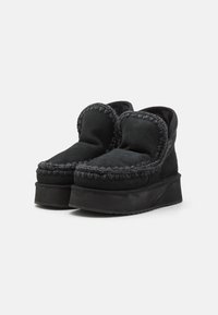 Zwarte instapschoenen met een dikke zool, voorzien van een gestructureerde stof, decoratieve stiksels langs de bovenrand en een afgerond ontwerp.